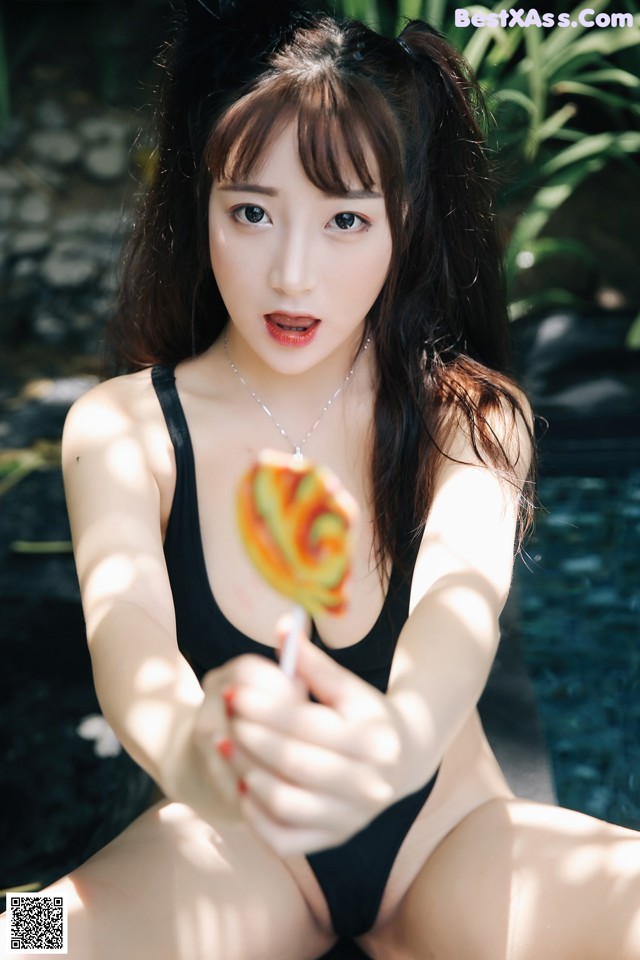 A woman in a black bathing suit holding a lollipop.