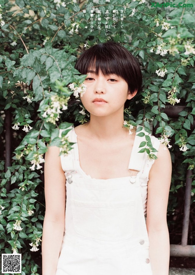 A woman in a white dress standing in front of a bush.