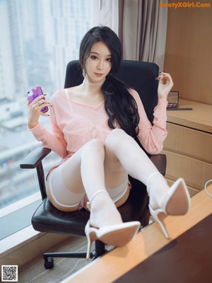 A woman in a pink dress and white stockings sitting on a couch.