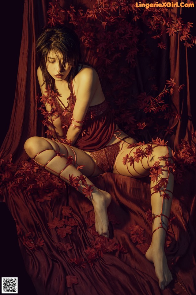 A woman in a red lingerie sitting on a bed of leaves.