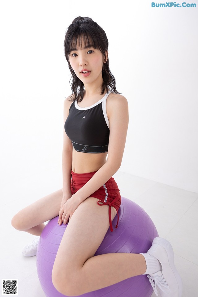 A woman sitting on an exercise ball wearing a black top and red shorts.