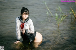 A woman in a school uniform sitting on a rock in the water.