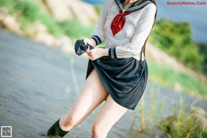 A woman in a school uniform sitting on a rock in the water.