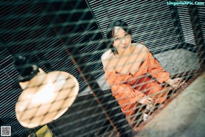 A woman in an orange dress sitting on a bench.