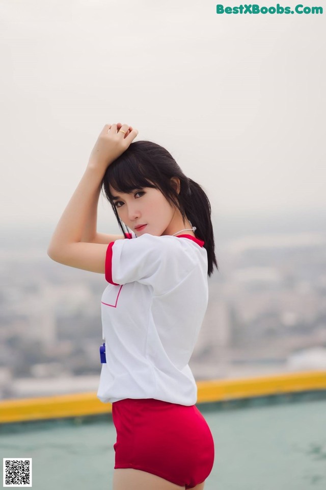 A woman in a white shirt and red shorts posing by a pool.