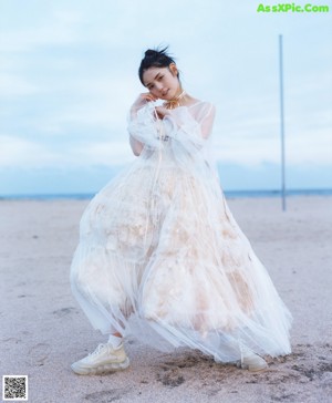 A woman in a white dress standing on a rock by the ocean.