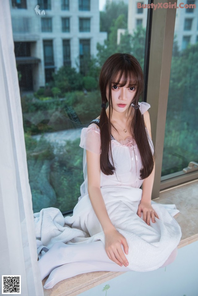 A woman sitting on a window sill in a white dress.