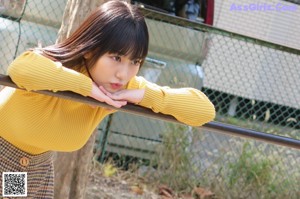 A young woman in a yellow sweater leaning on a railing.