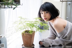 A woman in a gray sweater leaning against a window.