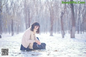 A woman in a white sweater and blue skirt holding a black bag.