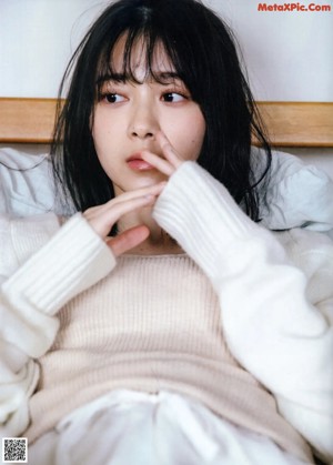 A woman with black hair and bangs leaning against a wall.