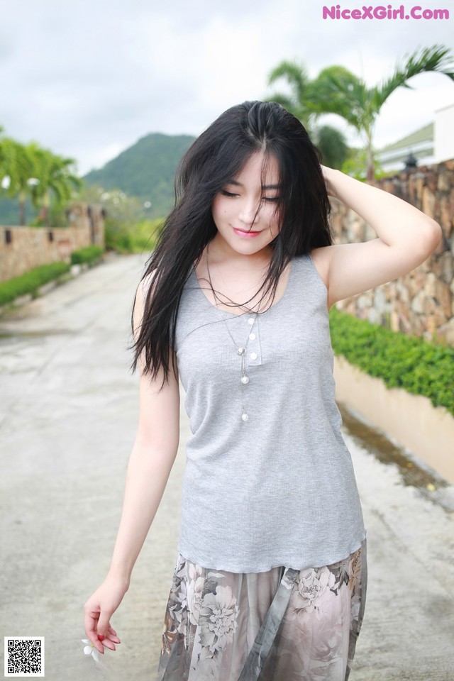 A woman in a gray tank top and floral skirt posing for a picture.