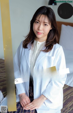 A woman in a white lab coat and black lingerie posing on a bed.