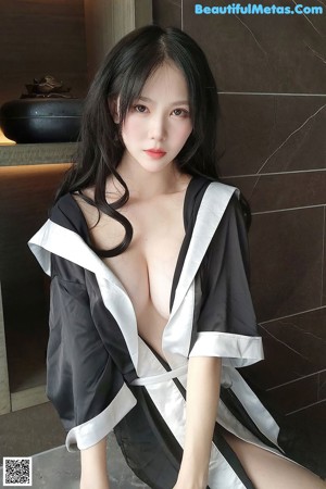 A woman in a black and white robe sitting on a bathtub.